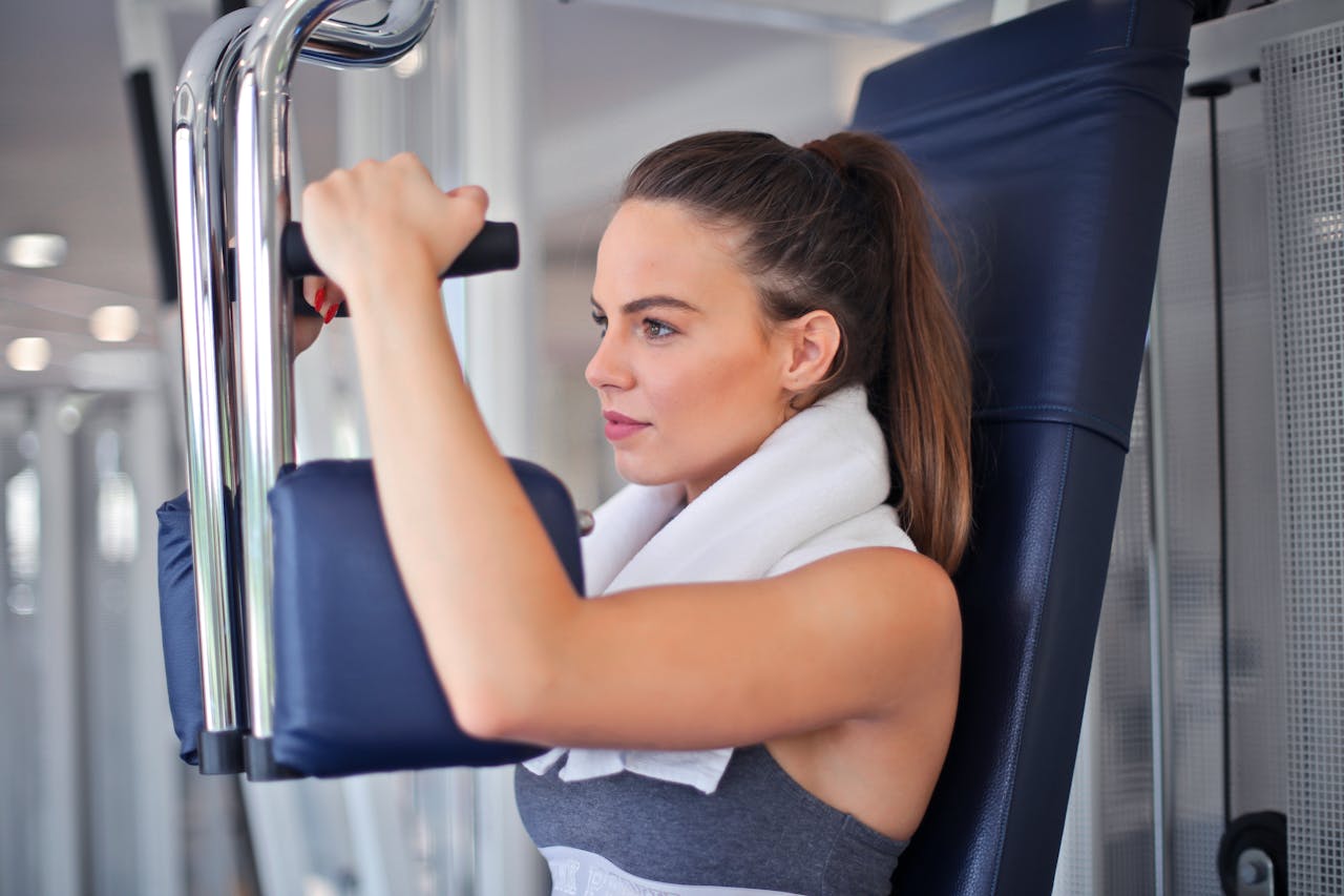 Young woman working out on a chest press machine in the gym, showing strength and determination.