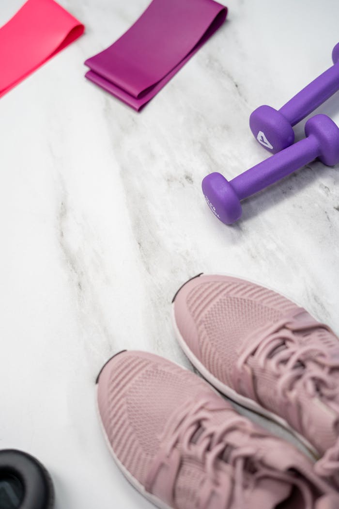 contact-img Flat lay of pastel pink fitness gear including sneakers and dumbbells on marble texture.